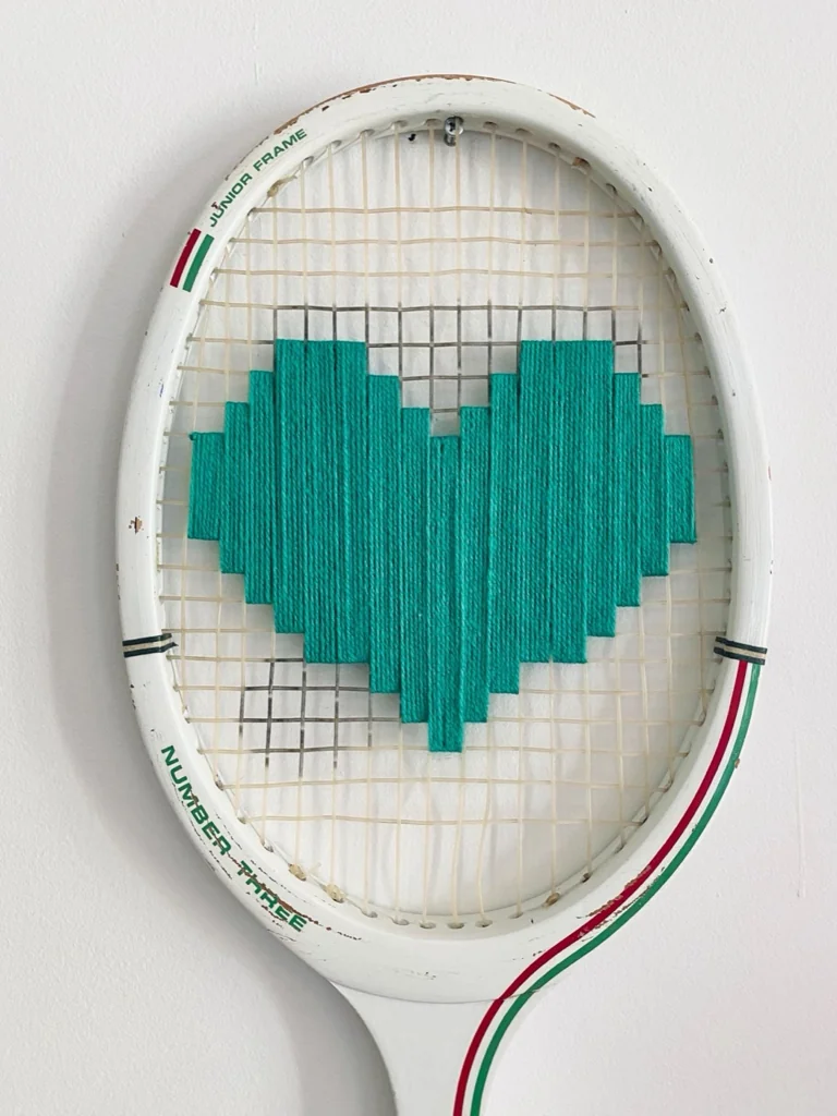 Gros plan de la broderie du cœur pixel vert dans le cordage d'une raquette de tennis vintage en bois