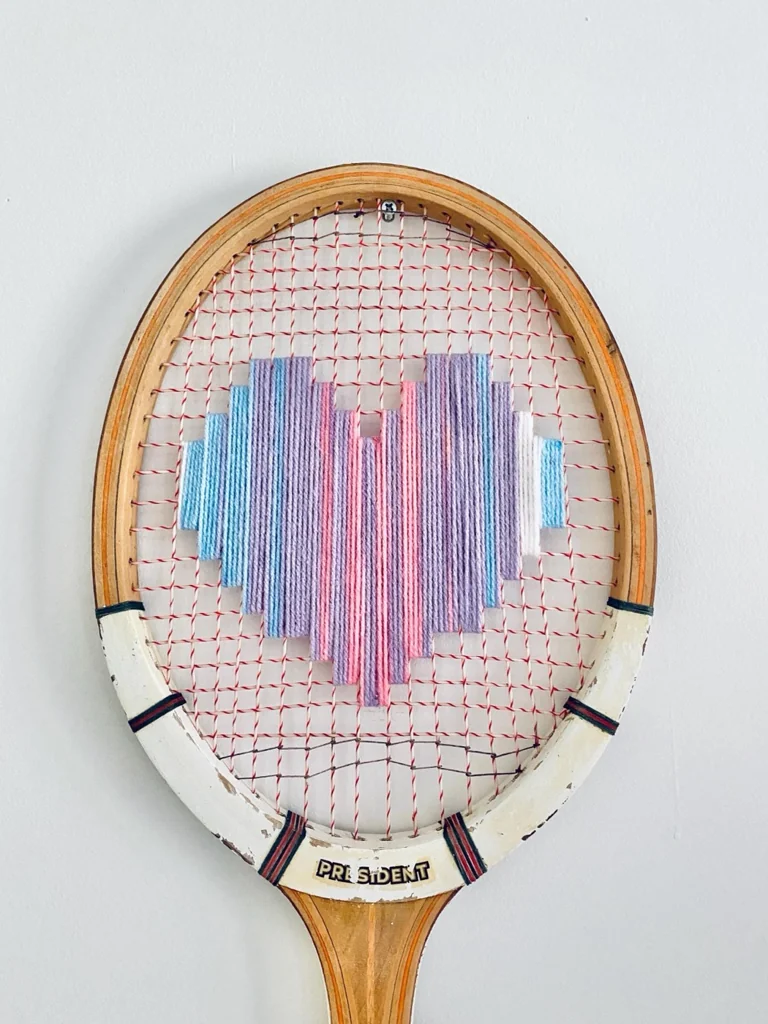 Gros plan de la broderie du cœur pixel pastel multicolore dans le cordage d'une raquette de tennis vintage en bois