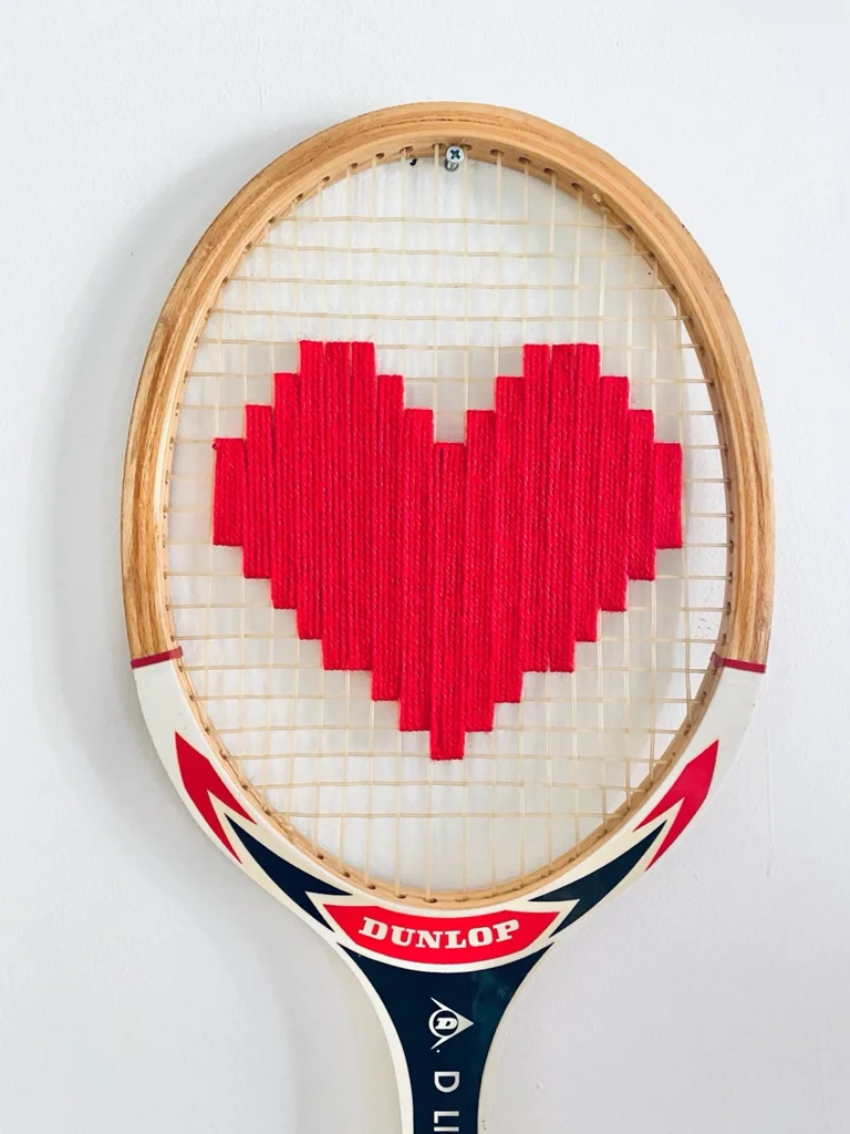 Gros plan de la broderie du cœur pixel rouge dans le cordage d'une raquette de tennis vintage en bois