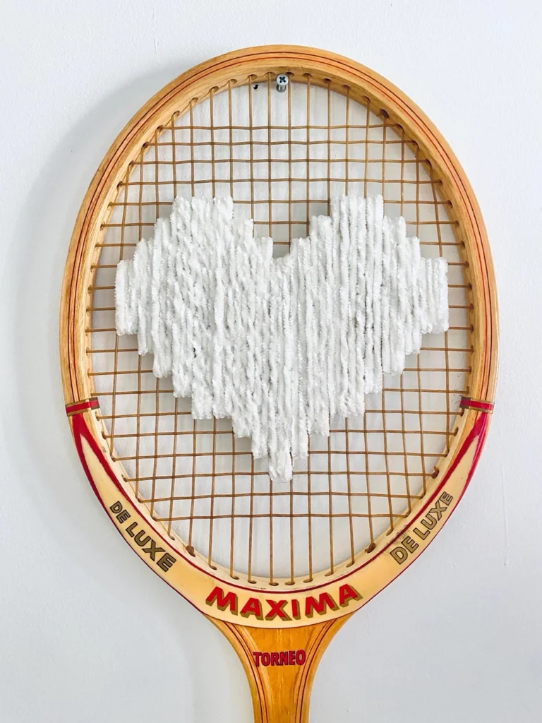 Gros plan de la broderie du cœur pixel blanc velours dans le cordage d'une raquette de tennis vintage en bois