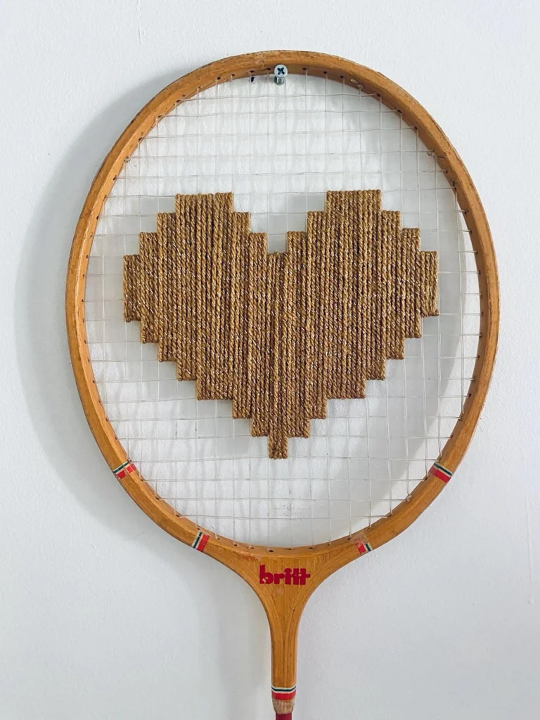 Gros plan de la broderie du cœur pixel doré caramel dans le cordage d'une raquette de badminton vintage en bois