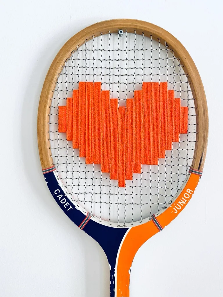 Gros plan de la broderie du cœur pixel orange dans le cordage d'une raquette de tennis vintage en bois