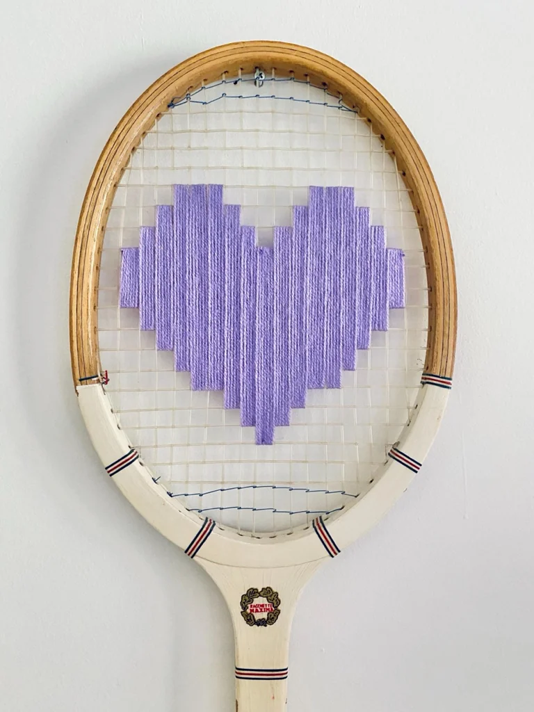 Gros plan de la broderie du cœur pixel lavande dans le cordage d'une raquette de tennis vintage en bois