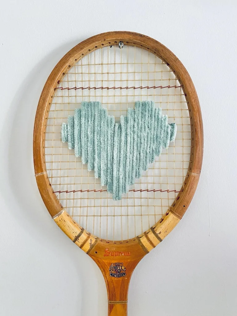 Gros plan de la broderie du cœur pixel vert pastel dans le cordage d'une raquette de tennis vintage en bois