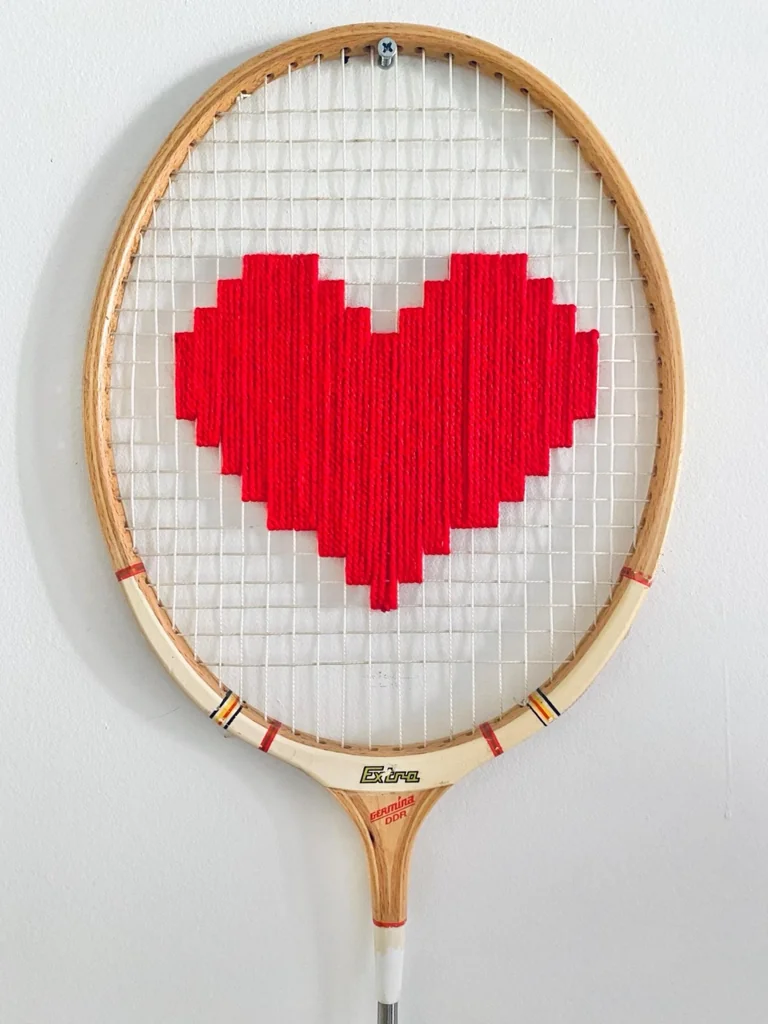 Gros plan de la broderie du cœur pixel rouge, au col blanc et au manche noir dans le cordage d'une raquette de badminton vintage en bois