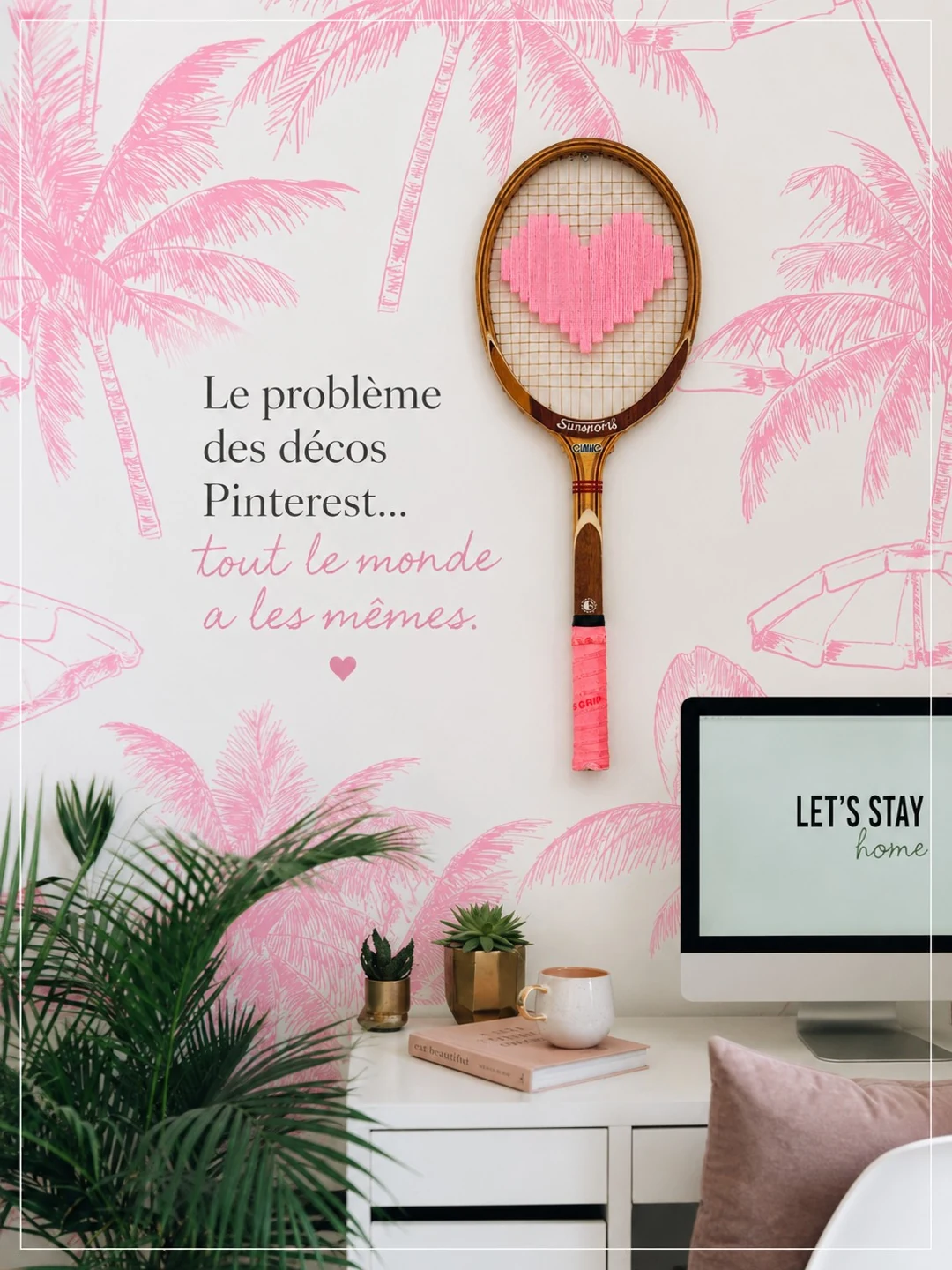 Raquette vintage au cœur rose brodé sur un mur aux motifs de palmiers roses, au-dessus d’un bureau