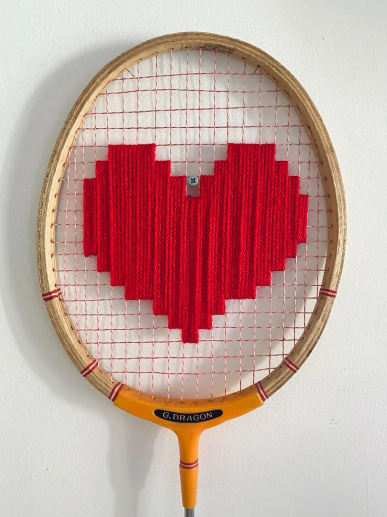 Gros plan de la broderie du cœur pixel rouge dans le cordage d'une raquette de badminton vintage en bois